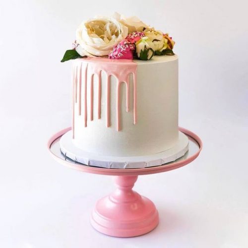 Celebration cake decorated with white icing a pink drip icing and flowers.