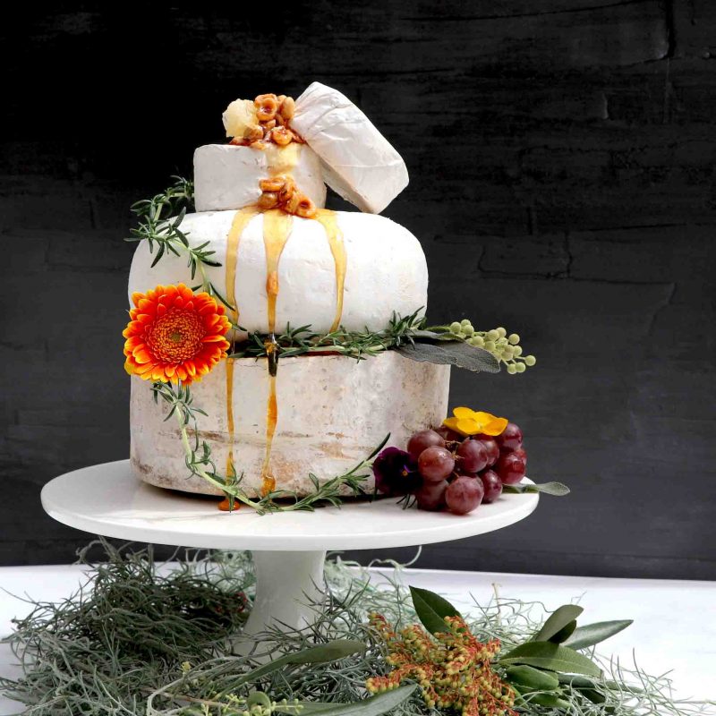 Gorgeous cheese tower made with various cheeses including brie and camembert stacked on top of each other decorated with figs, honey and fruit.